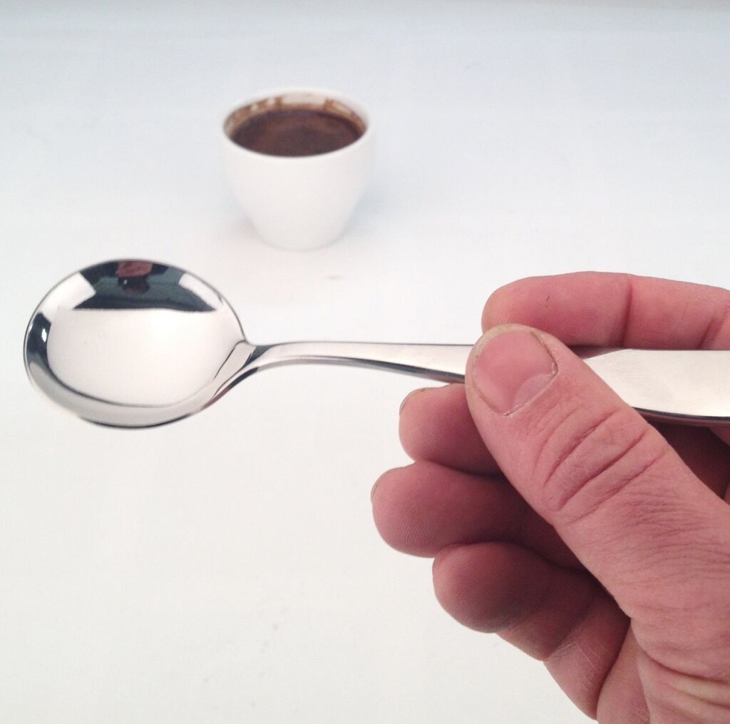 JoeFrex cupping lepel in de hand bij een kop koffie